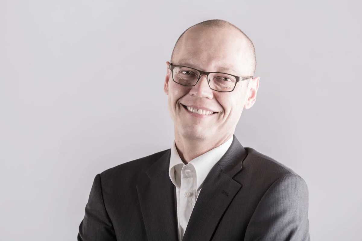 Portrait von David Rippmann, ein Mann mittleren Alters mit Brille in einem schwarzen Sacko